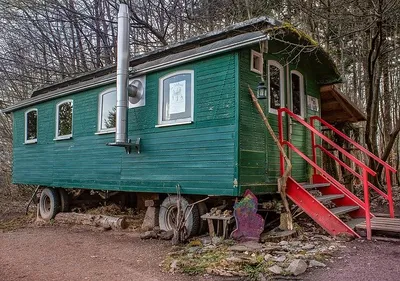 Grün gestrichener Bauwagen am Waldrand mit roter Holztreppe